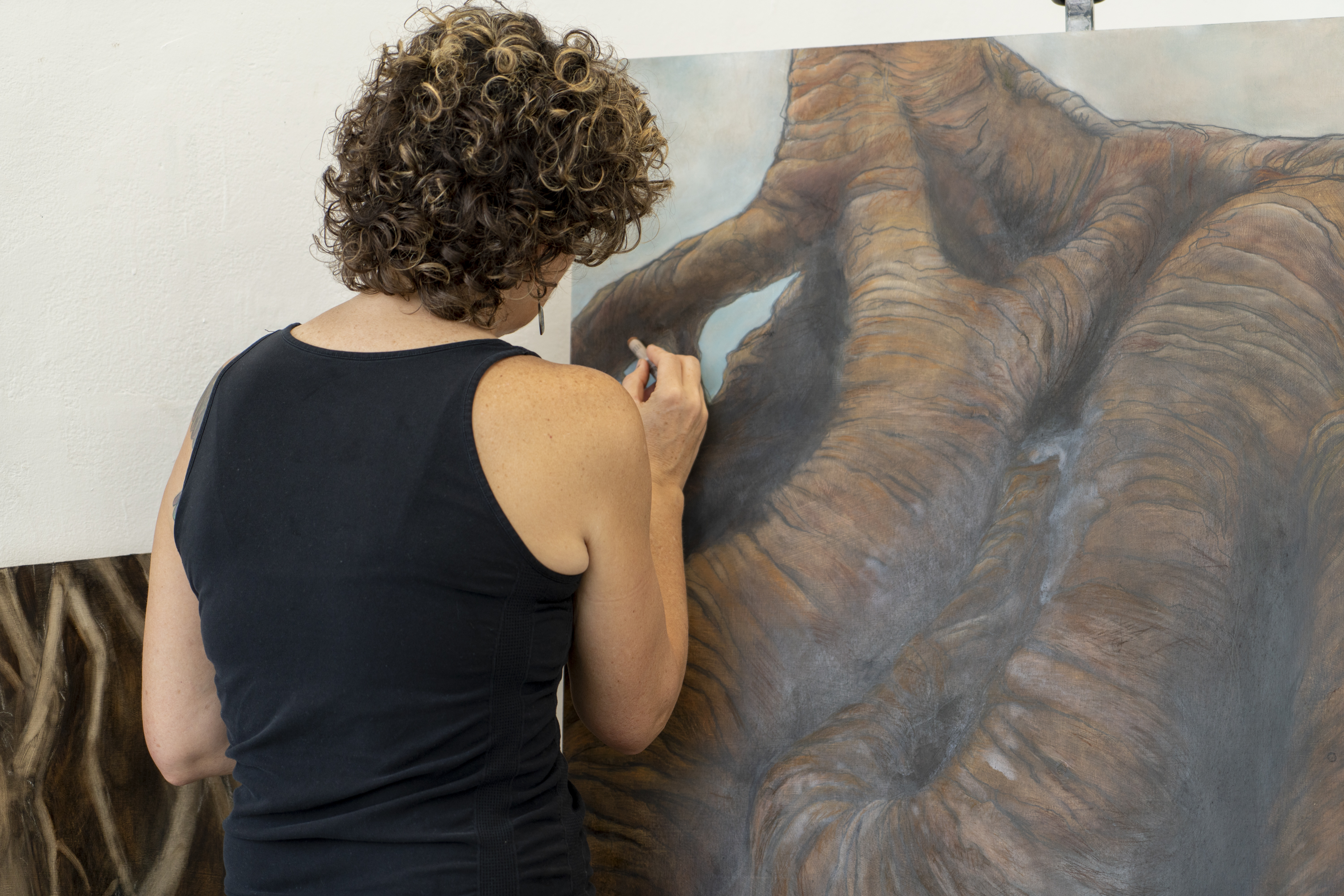 Adult artist drawing in brown chalk with their back to the viewer 