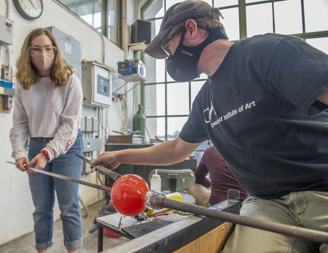 Student with instructor working with hot glass on a pipe